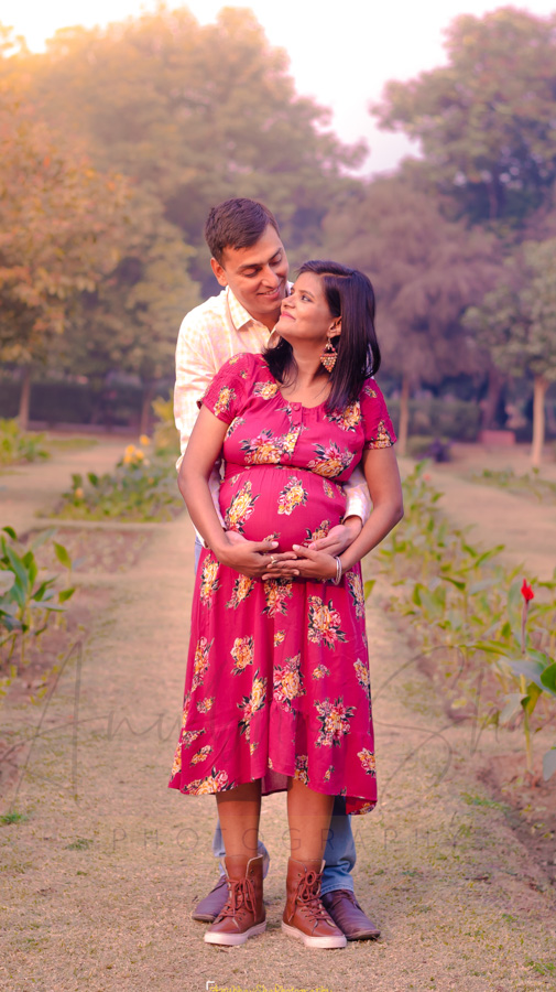 Indian couple posing for maternity baby shoot. The couple is posing in a  lawn with green grass and the woman is falunting her baby bump in Lodhi  Garden in New Delhi, India