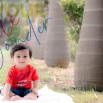 1 year happy sitter baby boy photoshoot outdoor garden wearing red tshirt blue denim