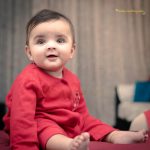 1 year sitting baby photoshoot indoor home wearing red romper smiling
