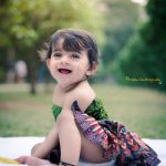 1 year sitting baby photoshoot outdoor garden green blue printed dress laughing happy pose