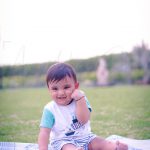 1 year sitting baby photoshoot outdoor garden white green dress shy pose with smile
