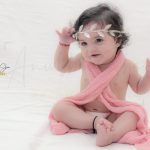 1 year sitting baby photoshoot indoor home pink wrapper with princess tiara theme smiling pose