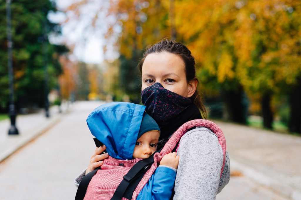 prevent babies from covid, mother holing baby in carrier outdoor wearing mask covid