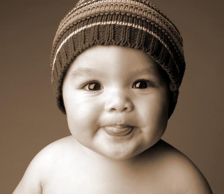 baby photoshoot at home sitter 1 year old naughty baby wearing a woollen cap with the tongue out and smiling