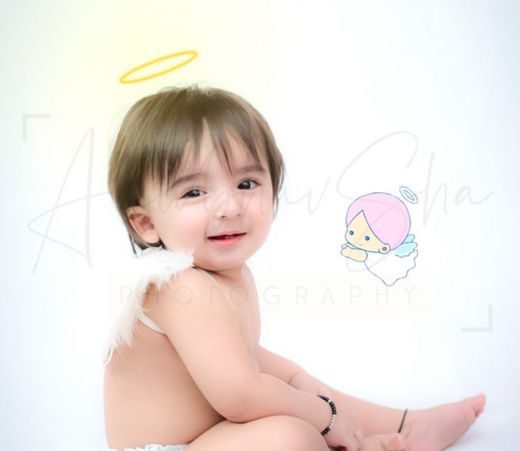 1 year sitting baby photoshoot indoor home with wings and angel silky hairs smiling