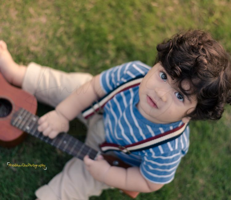 1 year sitting baby photoshoot outdoor garden guitar theme blue strip tshirt pants curly hairs