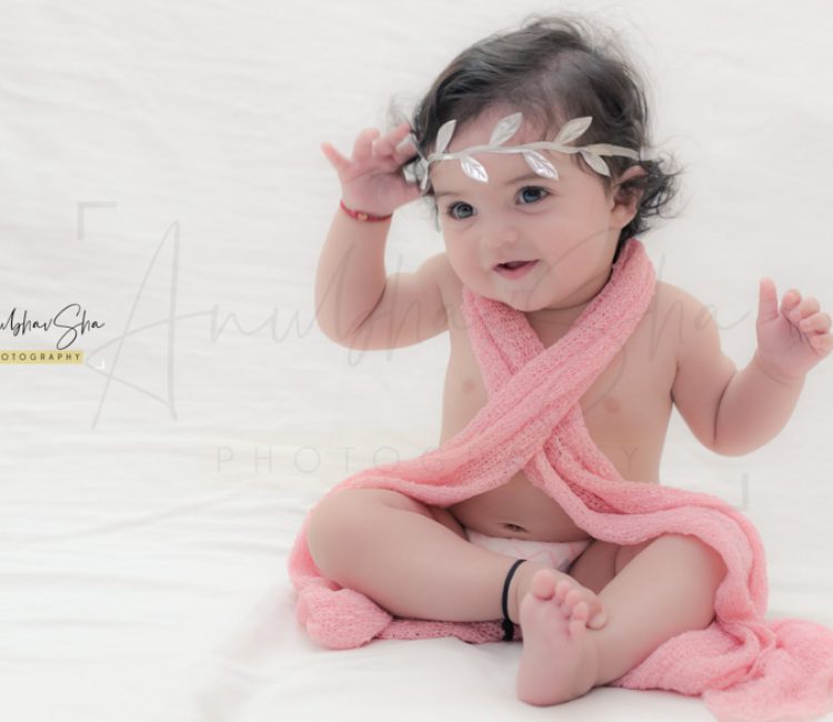 1 year sitting baby photoshoot indoor home pink wrapper with princess tiara theme smiling pose